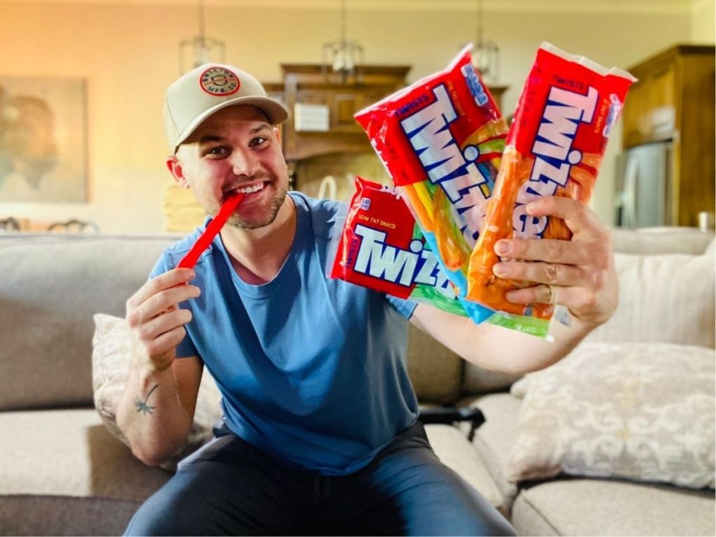 man eating twizzlers and holding up three twizzler bags
