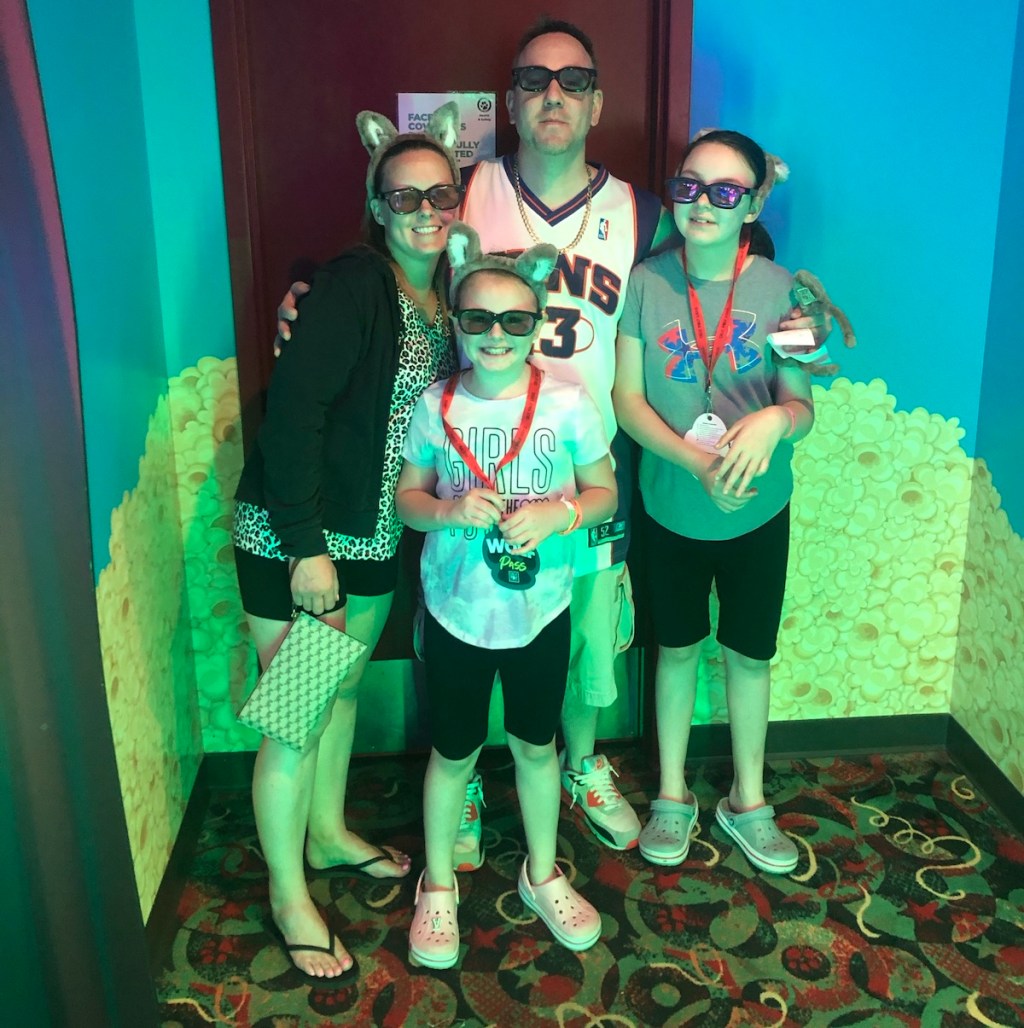 family of four standing together in neon colored room wearing sunglasses