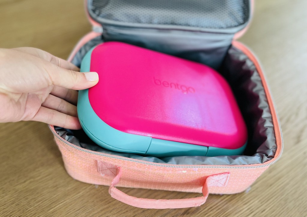 hand holding a hot pink bentgo bento lunchbox inside sparkly peach pink handle lunchbox