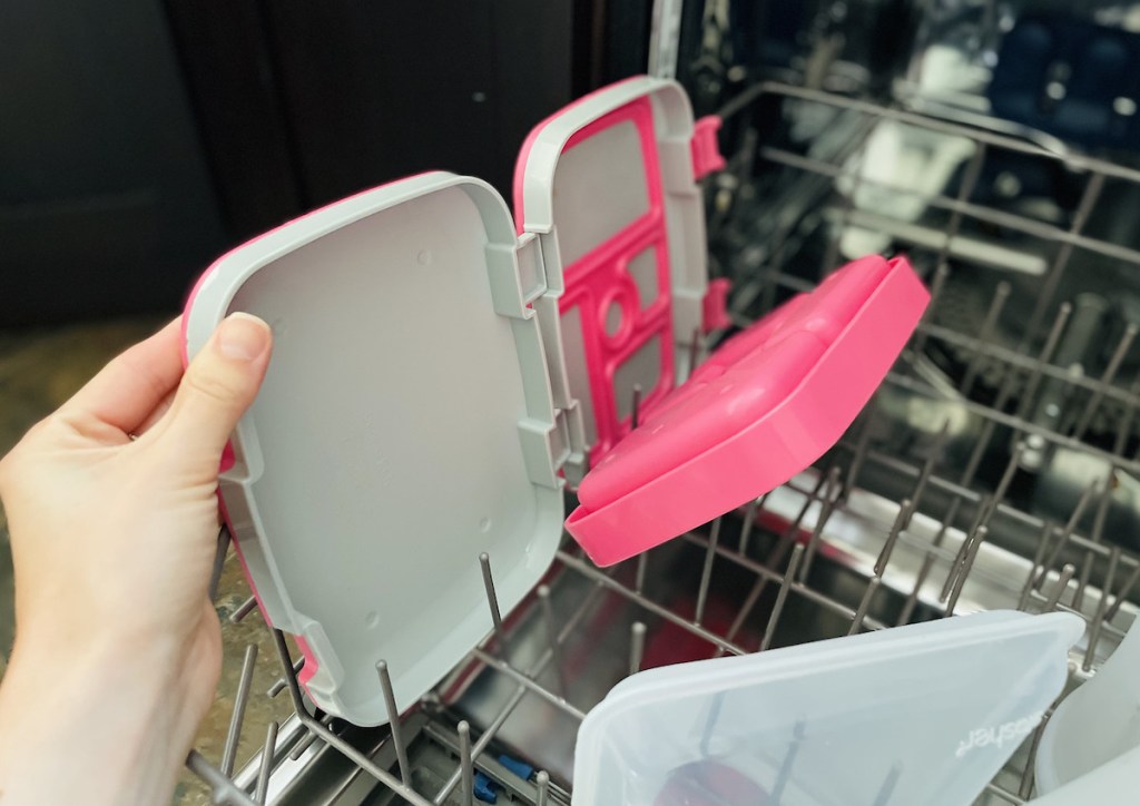 hand holding gray and pink bento lunchbox on dishwasher rack