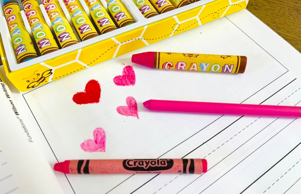 three different pink crayons with heart drawings laying on white paper