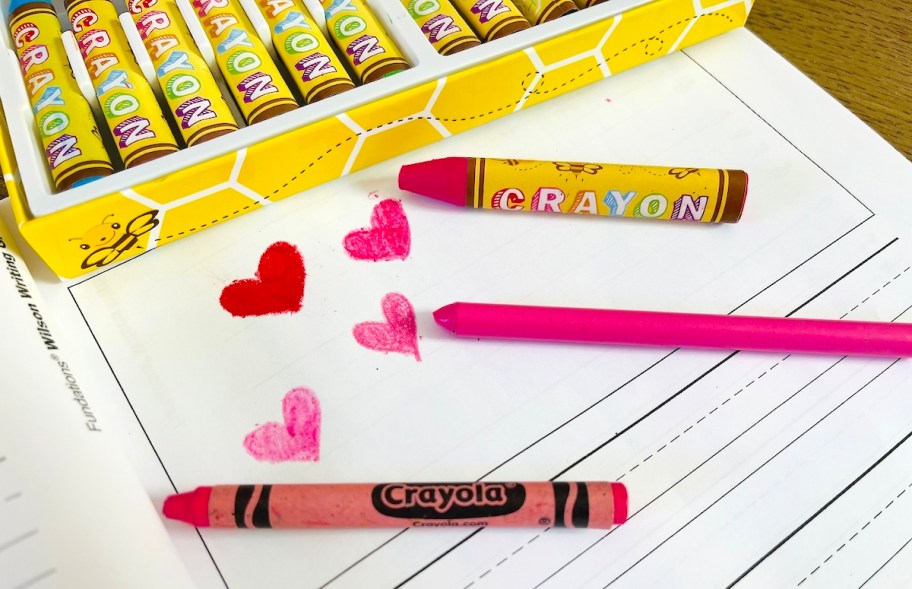 three different pink wax sticks with heart drawings laying on white paper