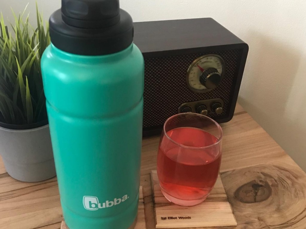 teal water bottle next to glass of red juice on small table