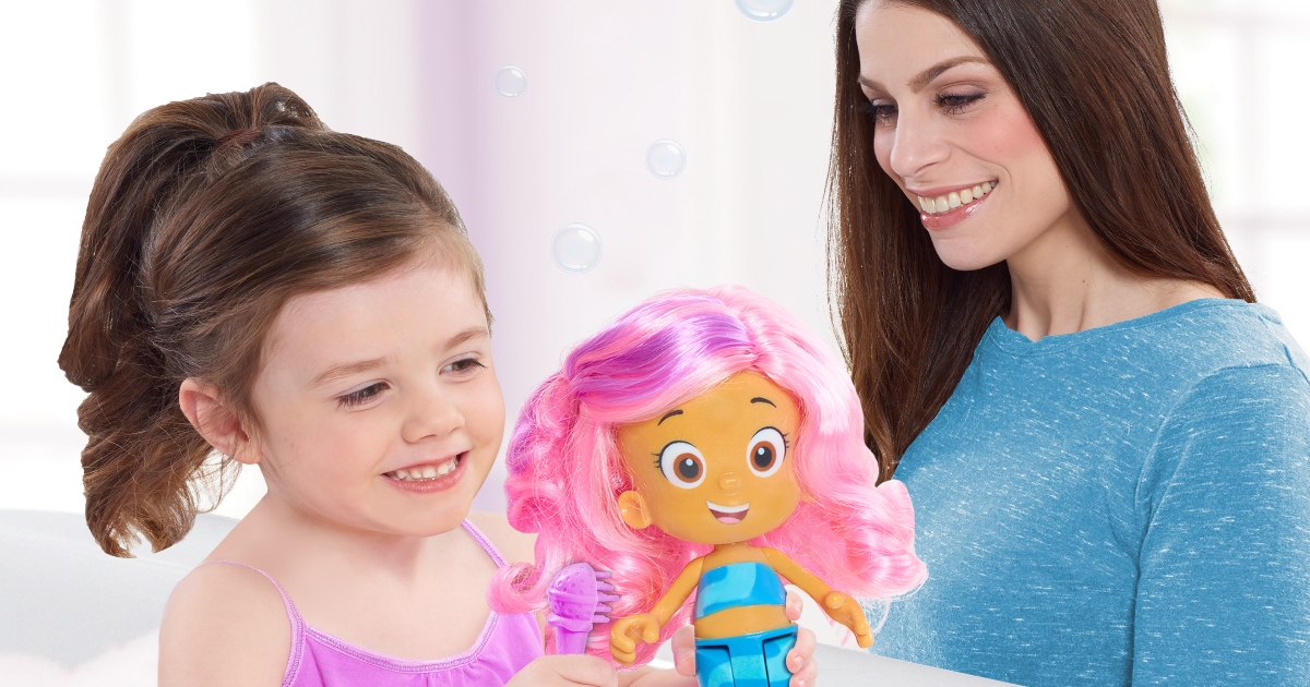 girl holding bubble guppies doll while her mom watches her play with it.
