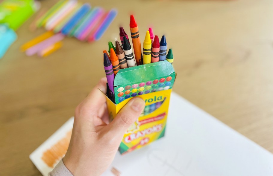 hand holding an open box of crayons 