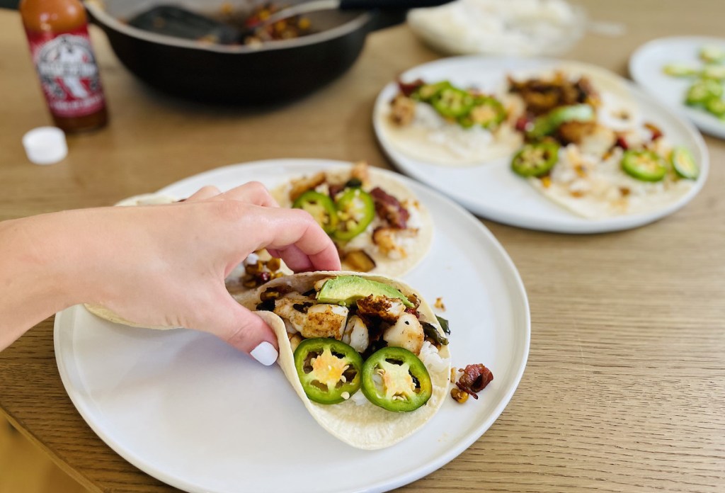 hand holding a fish taco on plate