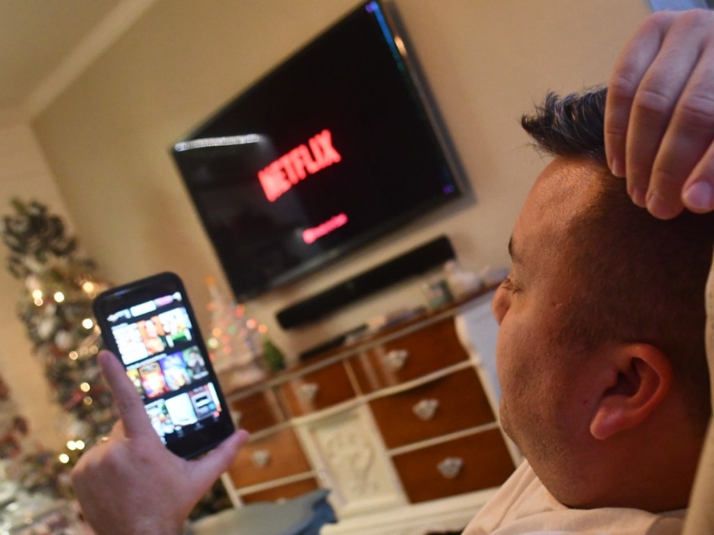 man streaming on phone in front of Netflix on TV