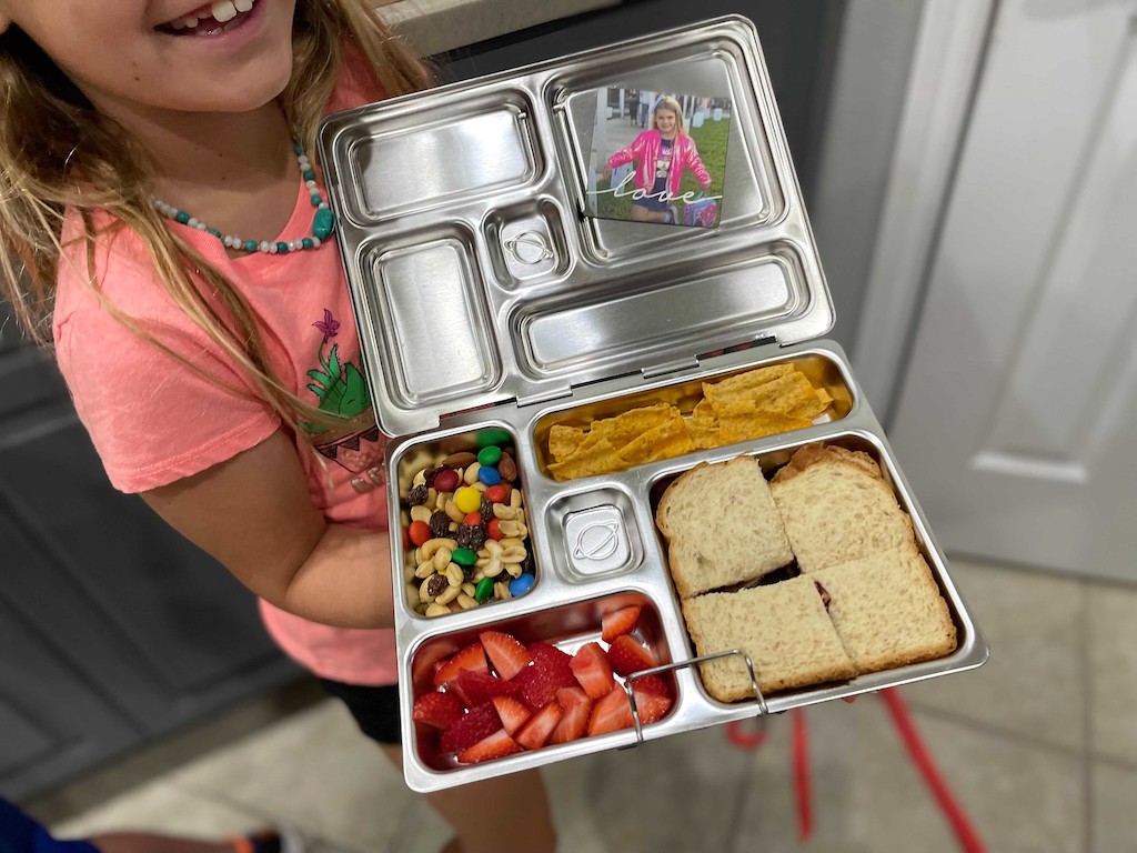 mała dziewczynka trzymająca metalowe pudełko na lunch w stylu bento Planetbox 
