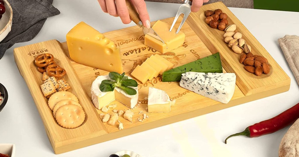 person slicing a piece of cheese on a charcuterie board with other cheeses and crackers