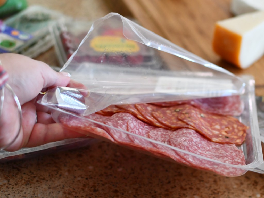 person holding an open package of salami