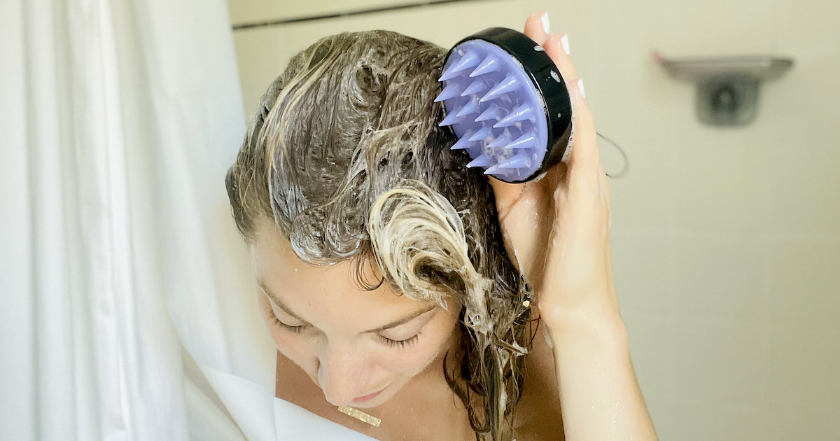woman holding scalp massager in shower with soapy hair