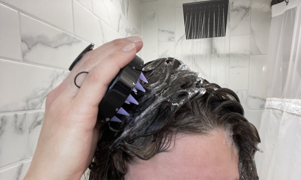 woman holding scalp massager to wet hair in shower