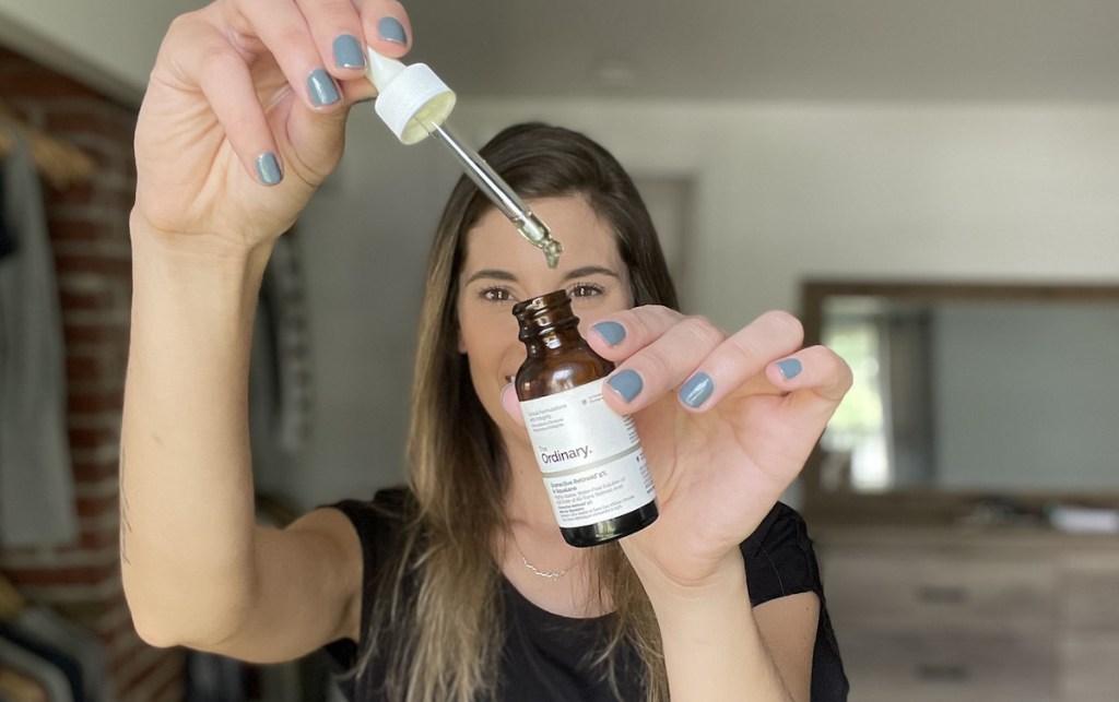 woman holding up amber bottle of retinoid in bedroom