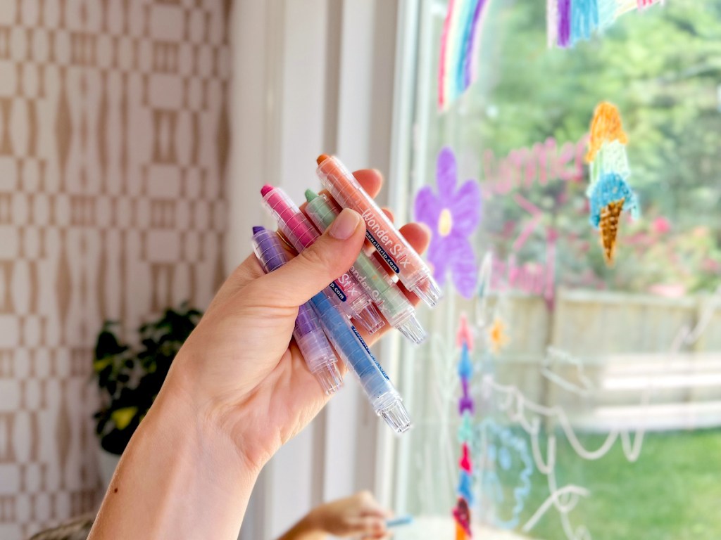hand holding stack of wonder stix crayons in front of kids decorating window
