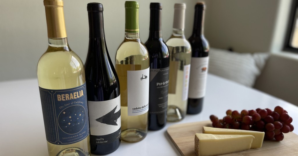 bottles of wine next to cheese and grapes