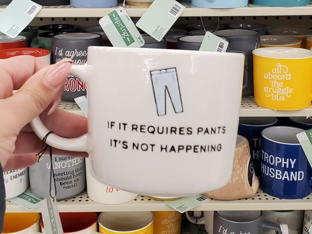 hand holding a coffee mug from Hobby Lobby that says it it requires pants, it's not happening