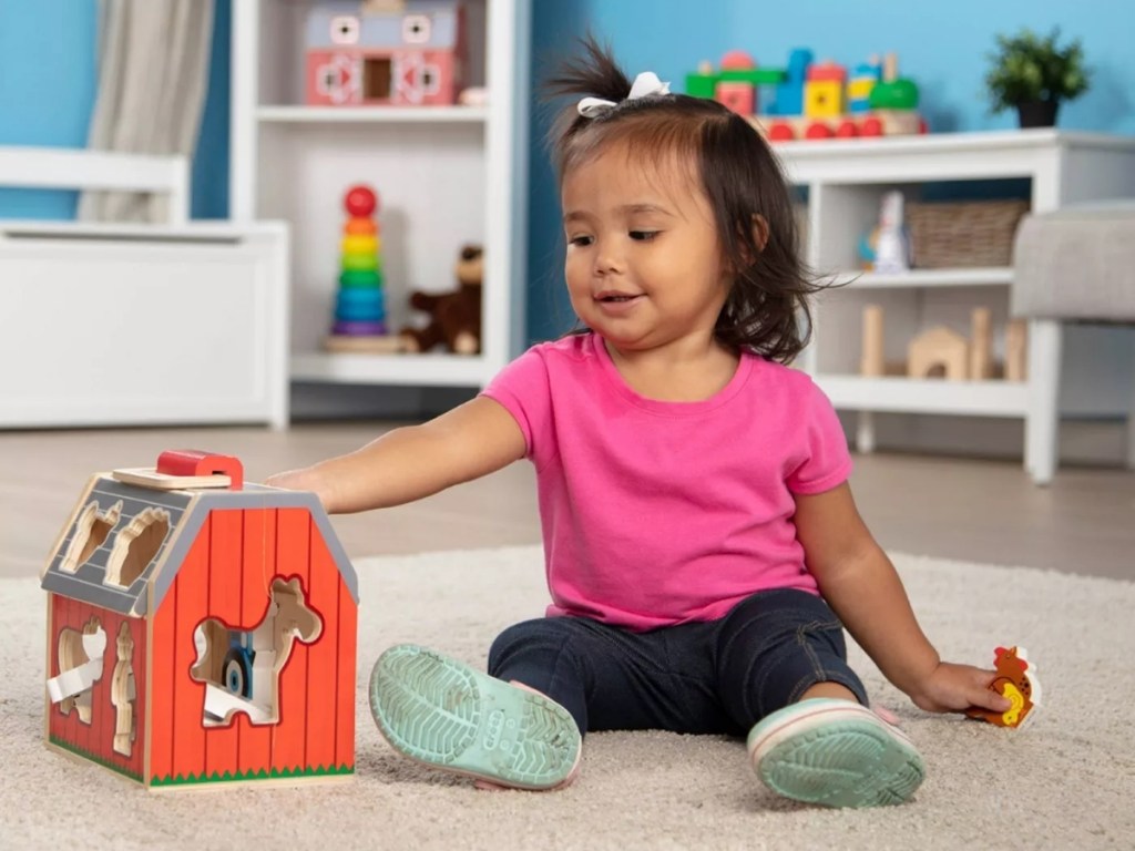 little girl playing with melissa and doug wooden barn