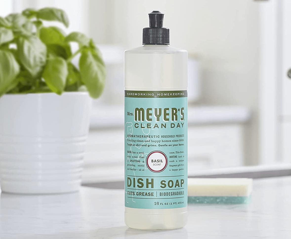 bottle of Mrs. Meyer's Dish Soap sitting on a counter in front of potted basil and a kitchen sponge