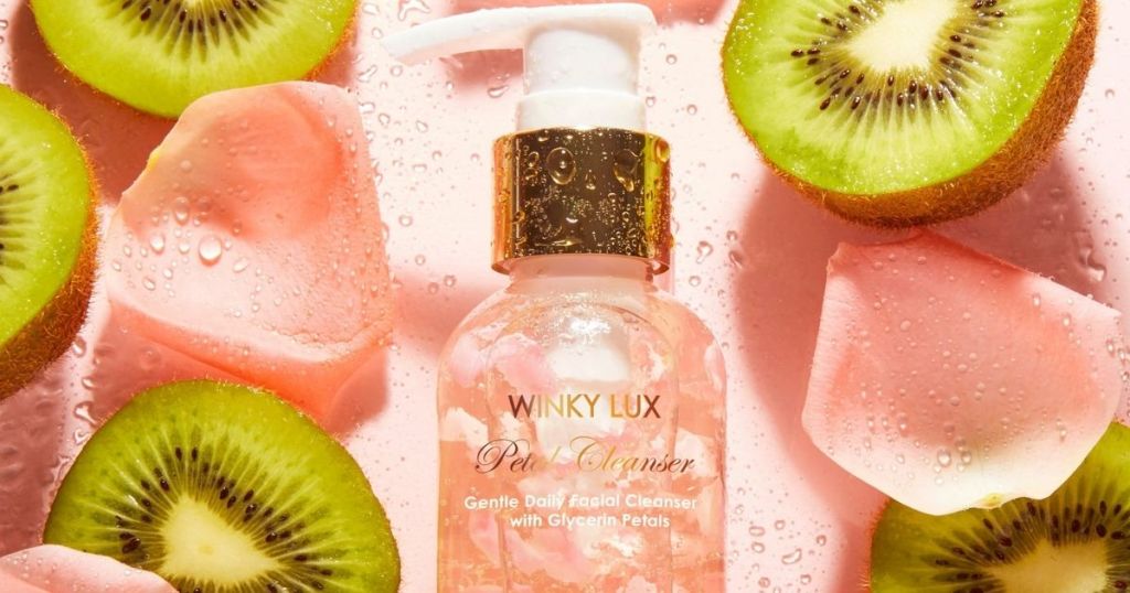 bottle of Winky Lux Petal Cleanser surrounded by kiwi and flower petals