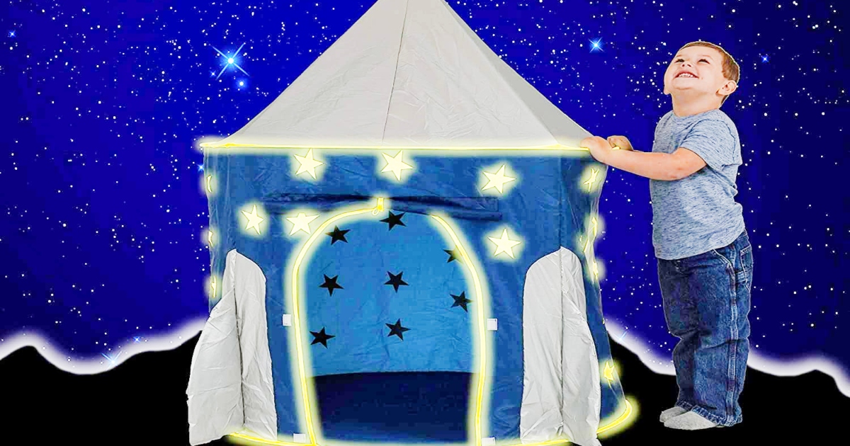 rocket ship tent set up against a night background and a young boy standing beside it