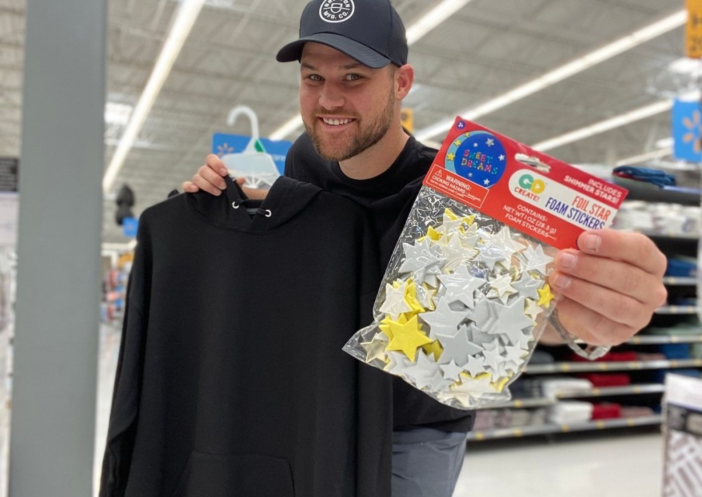 man holding pack of foam star stickers holding black hoodie on hanger