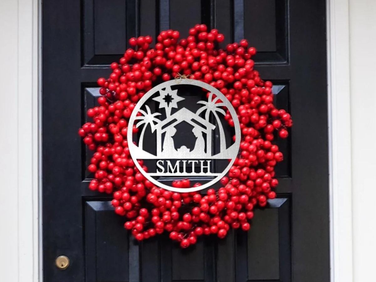 personalized name sign with nativity scene displayed in front of red wreath hanging on a black door