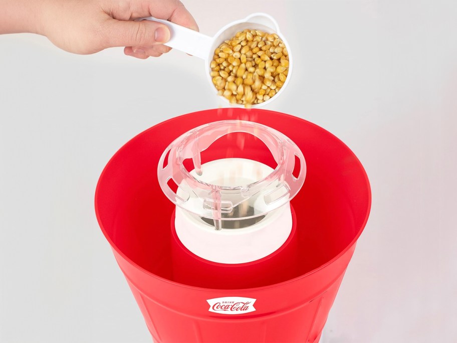hand pouring popcorn kernals into popper