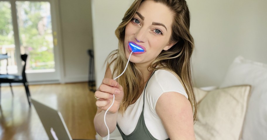woman wearing teeth whitener on couch with laptop