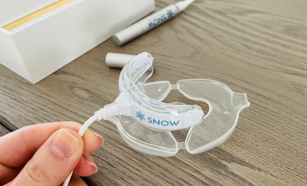 hand putting snow teeth whitening mouthpiece into clear storage tray