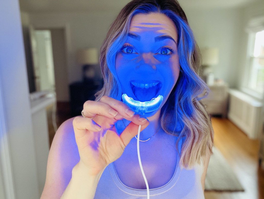 woman holding up blue light mouthpiece in front of open mouth