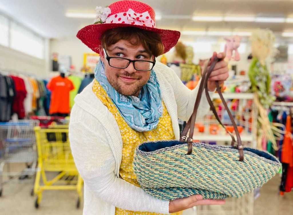 man dressed as old lady holding up bag