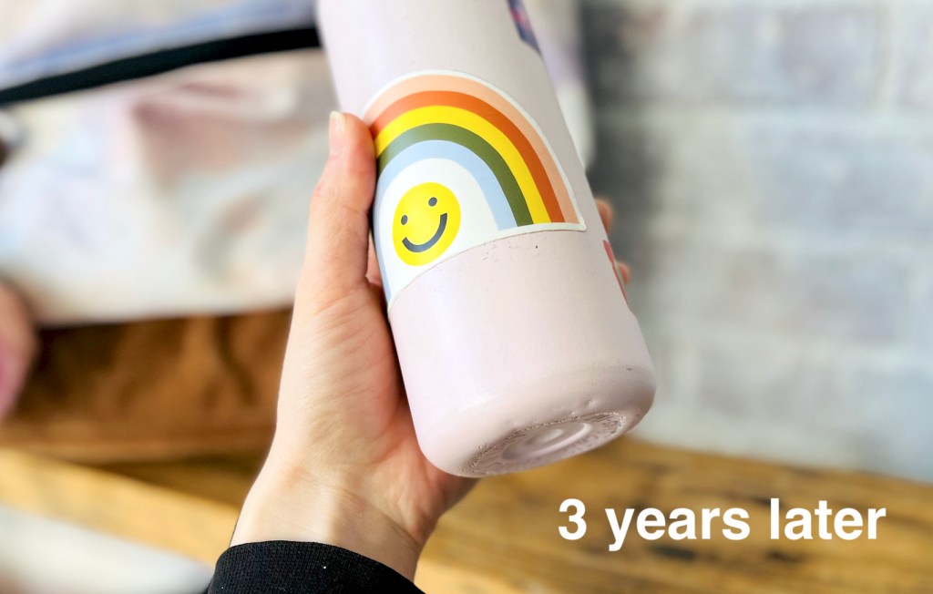 hand holding a takeya water bottle with rainbow smiley face sticker