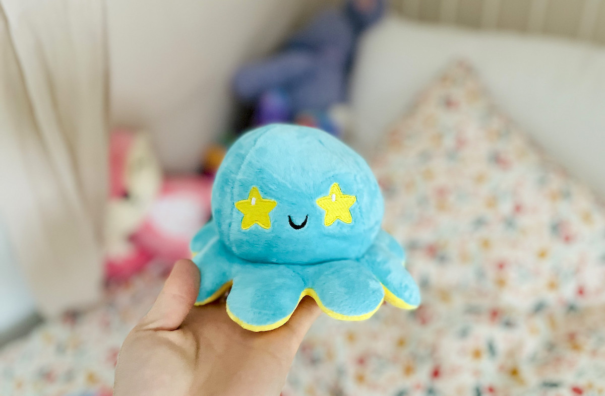 hand holding up blue and yellow stuffed teeturtle reversible octopus plush over kids flower bed
