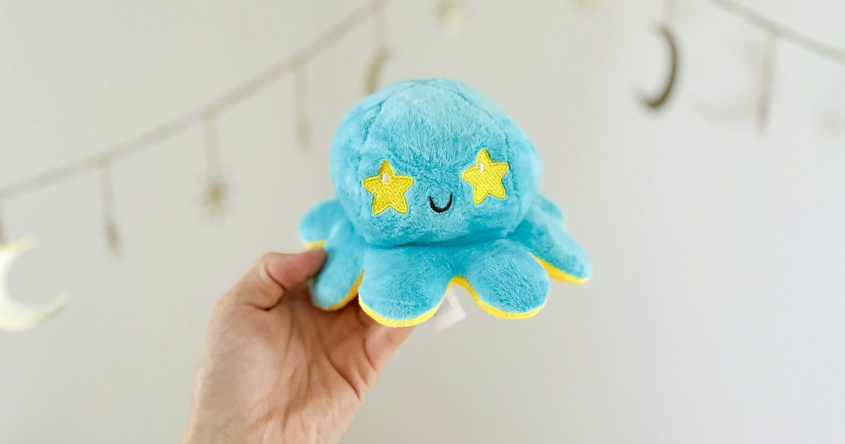 hand holding a blue and yellow reversible octopus in front of gold star banner