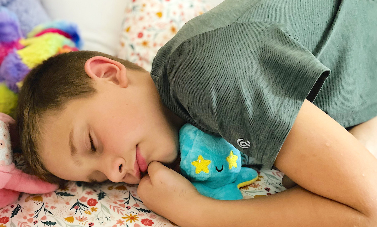 boy snuggling blue and yellow stuffed animal in bed sleeping