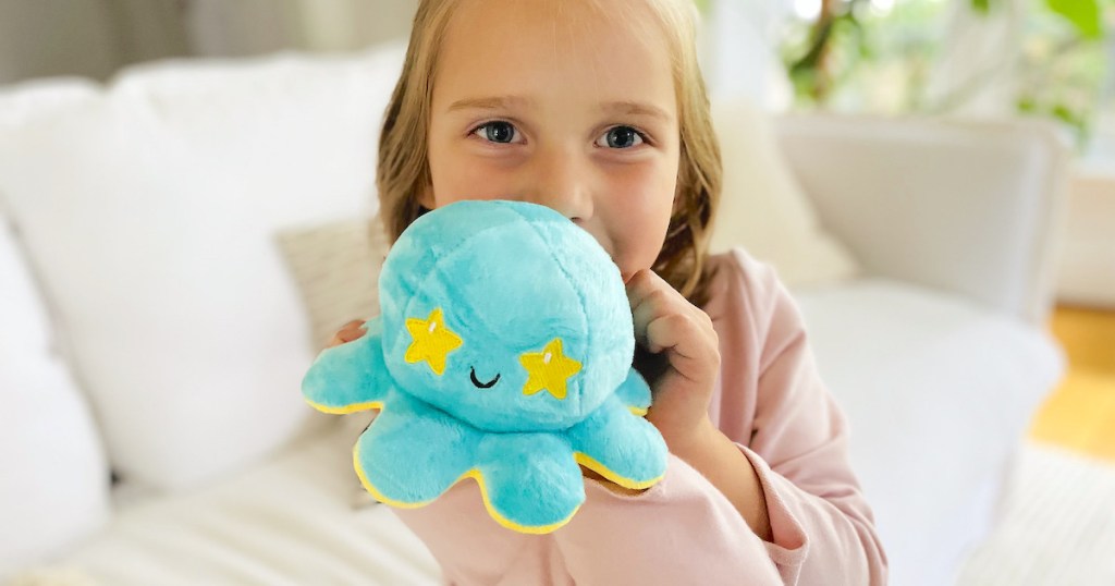girl holding blue and yellow Teeturtle reversible octopus sitting on white couch