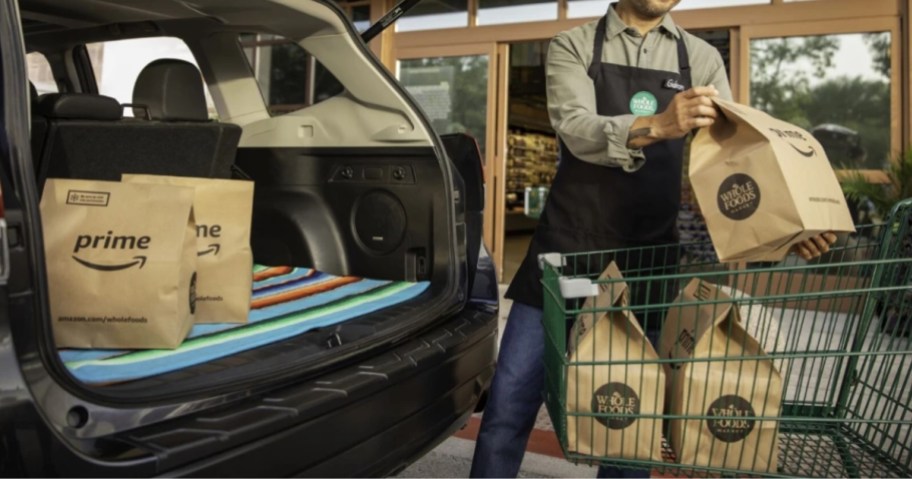 person scanning Amazon grocery items and placing into back of SUV 