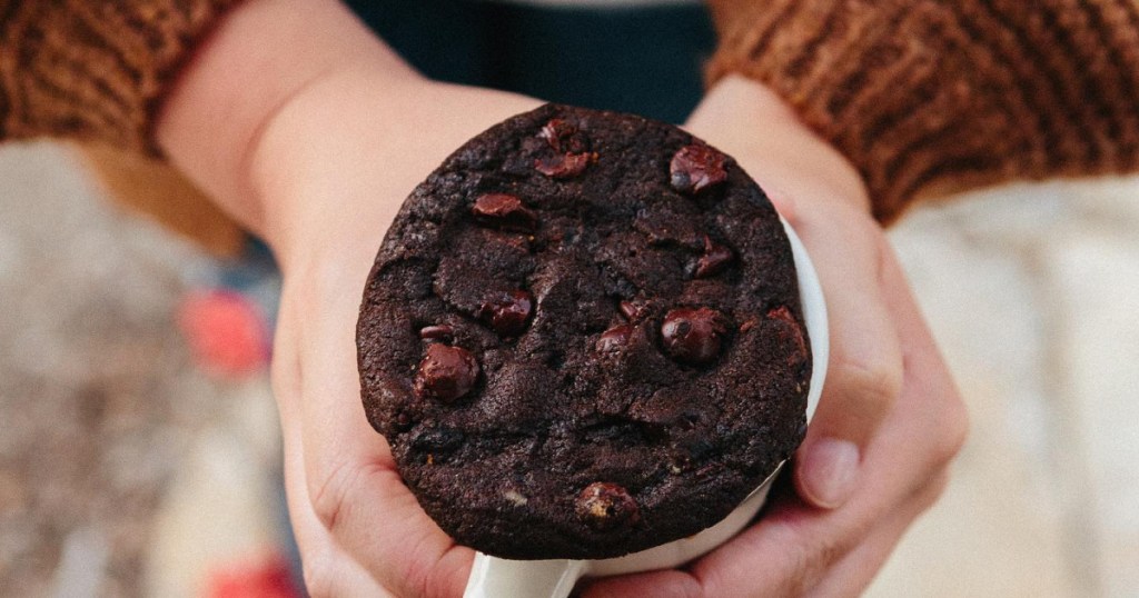 person holding a mug with a chocolate cookie on top