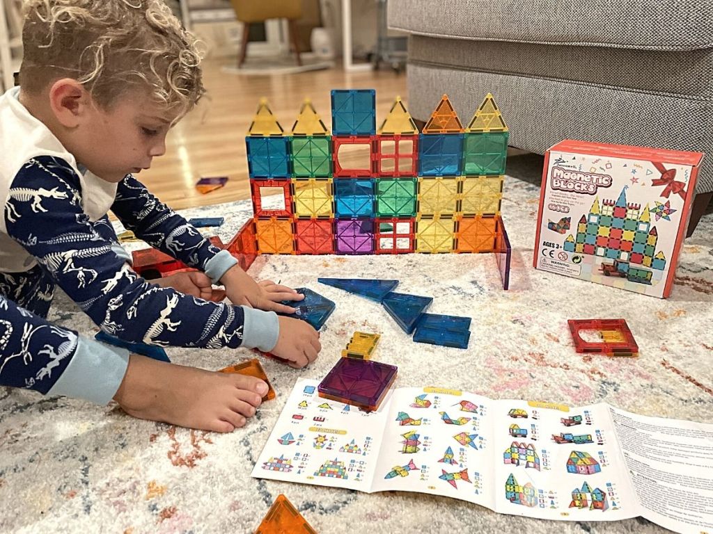 boy looking at idea book and building with magnetic tiles