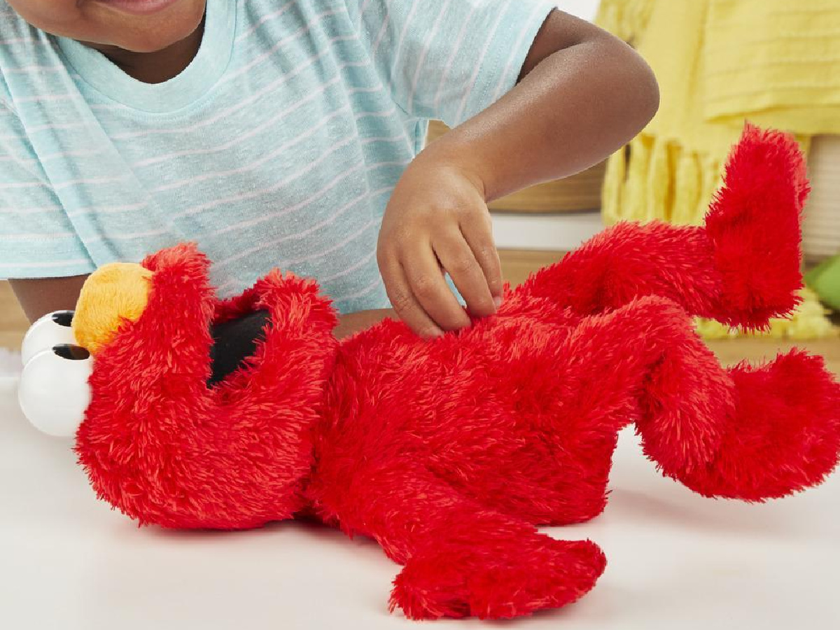 child tickling the belly of a tickliest tickle me elmo doll laying on a flat surface