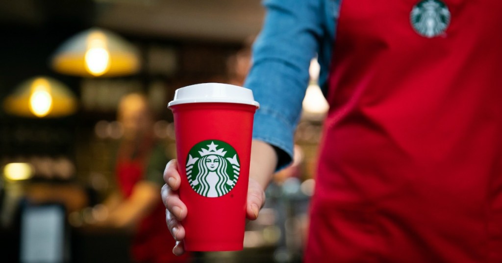 Starbucks employee holding out red Starbucks holiday cup