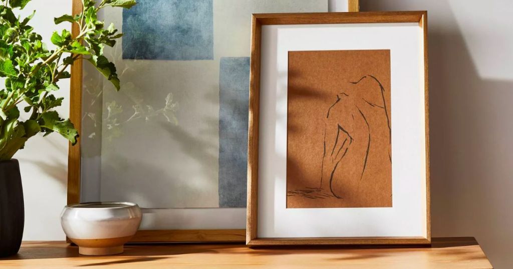 Woman Figural Sketch Framed Wall Art propped against another paiting sitting on top of a console table
