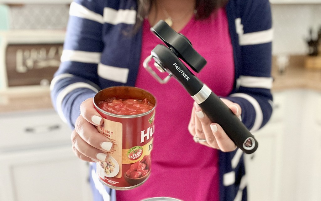 woman holding a can of tomatoes and black can opener in kitchen