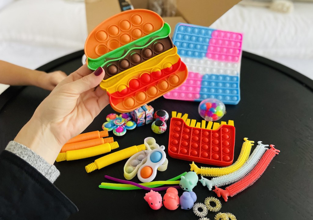 hand holding cheeseburger silicone toy with other various toys on table