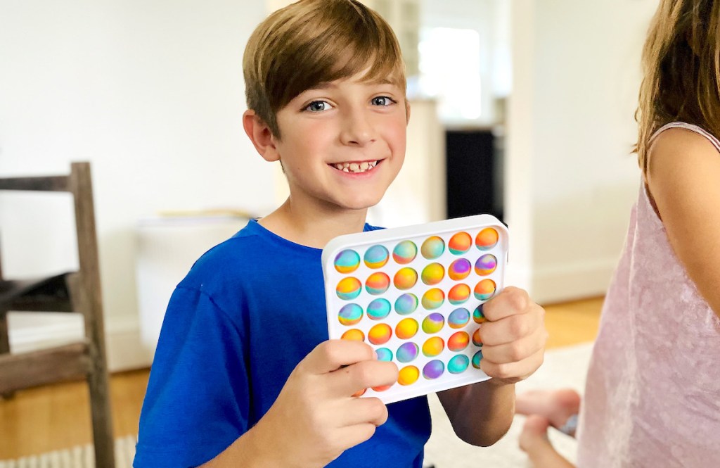 boy holding up white and tie dye pop it toy smiling