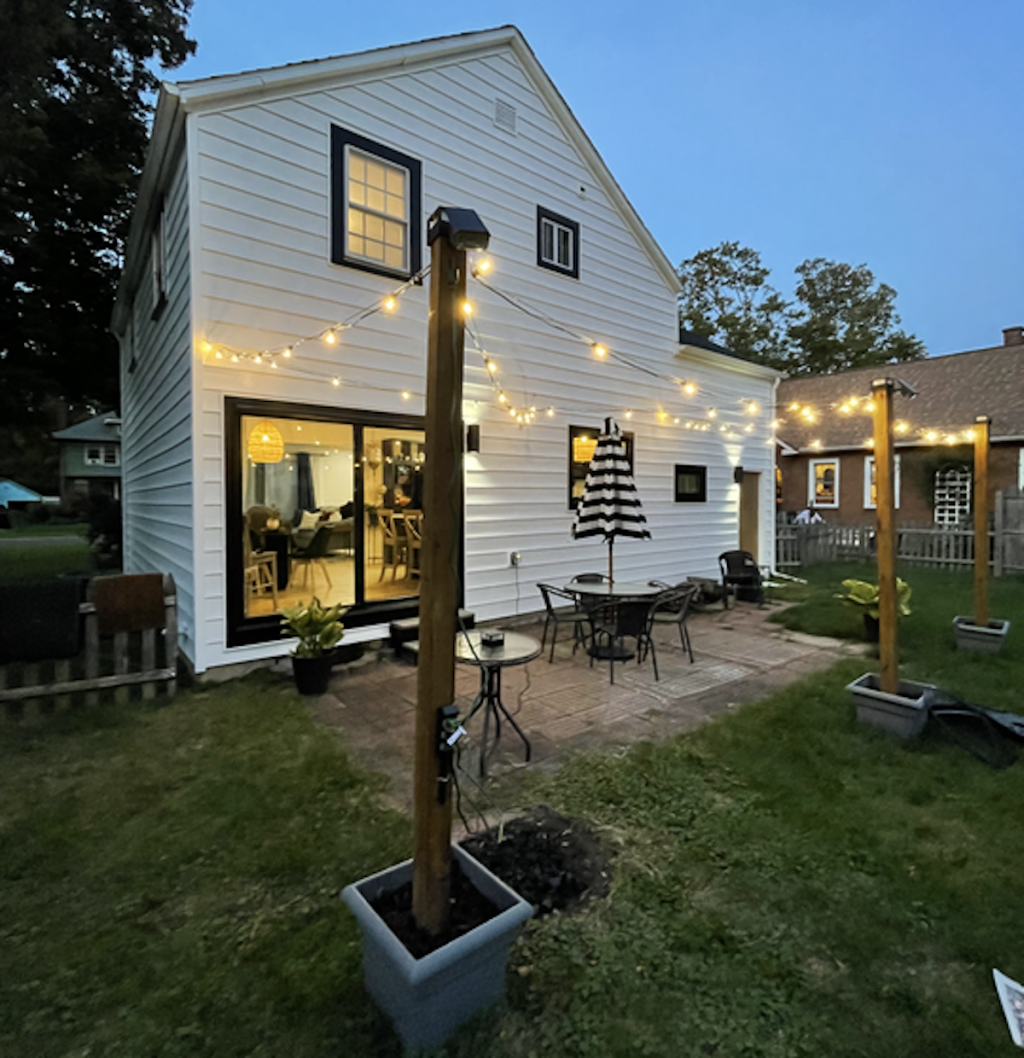 back of white and black house with footers and string lights in dark