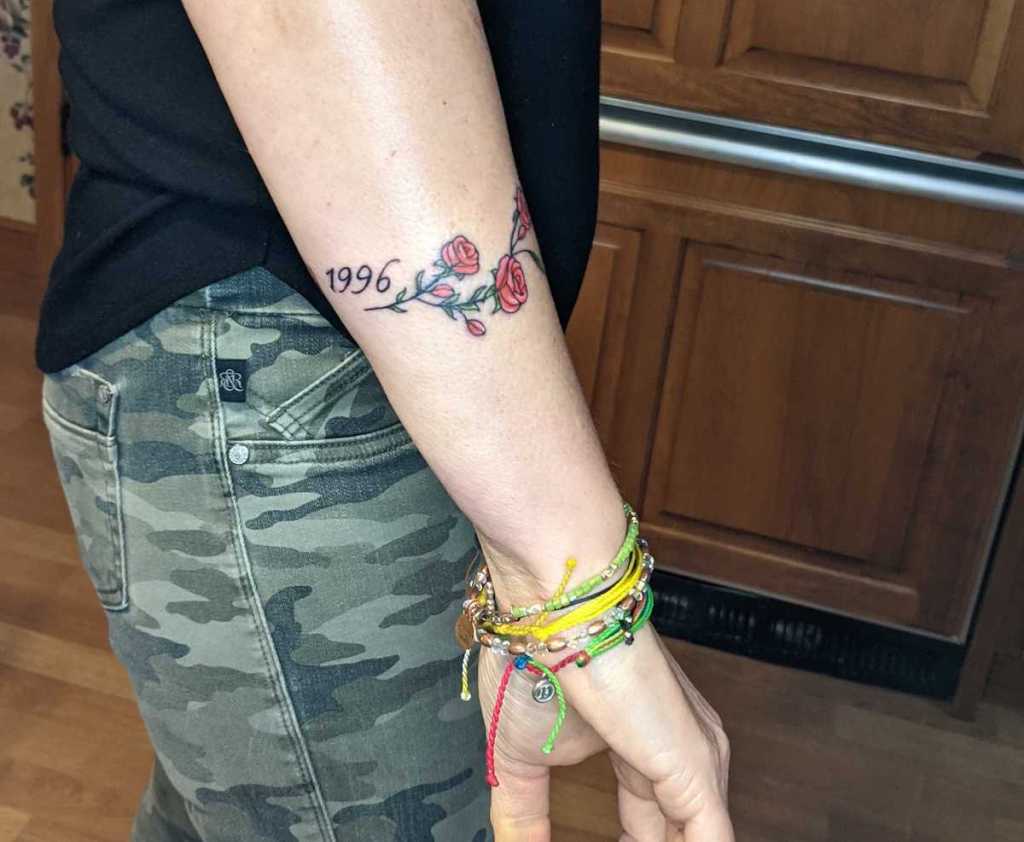 woman arm with roses and year tattoo on side arm 