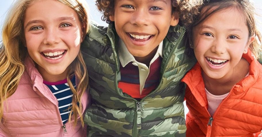 three kids in outerwear smiling for a pic