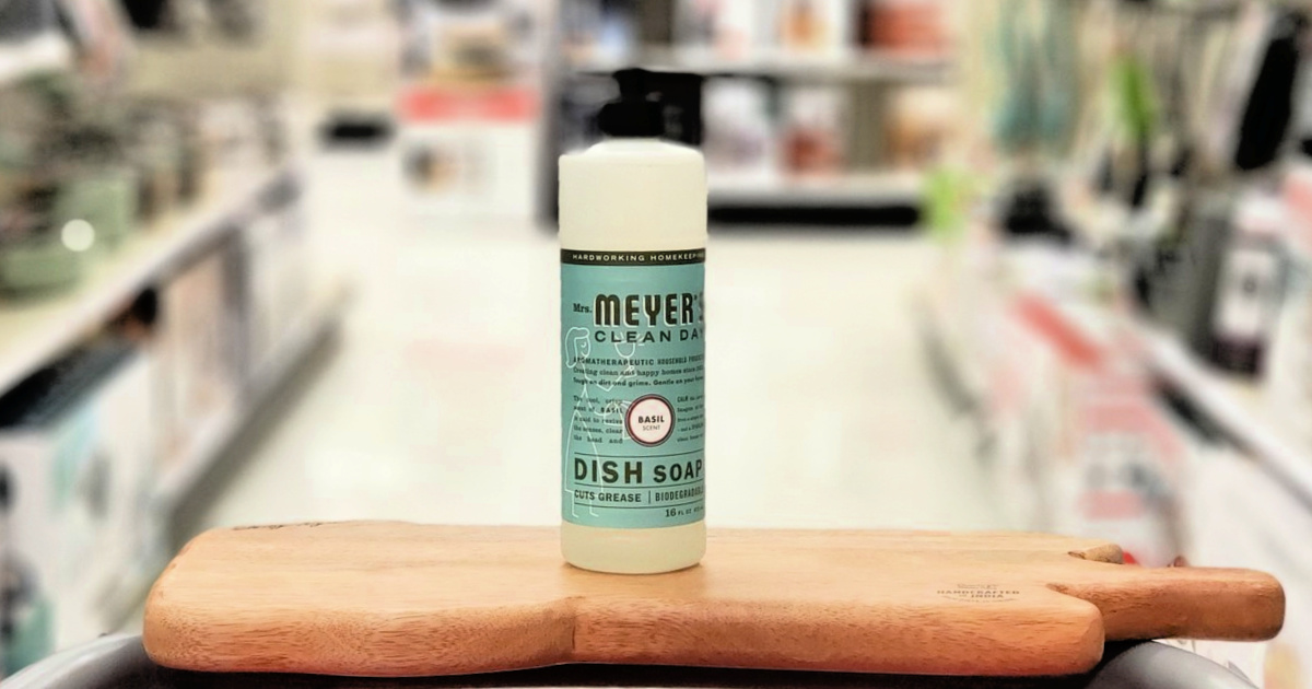 bottle of Mrs. Meyer's Dish Soap sitting on a rustic wooden cutting board in front of a store aisle