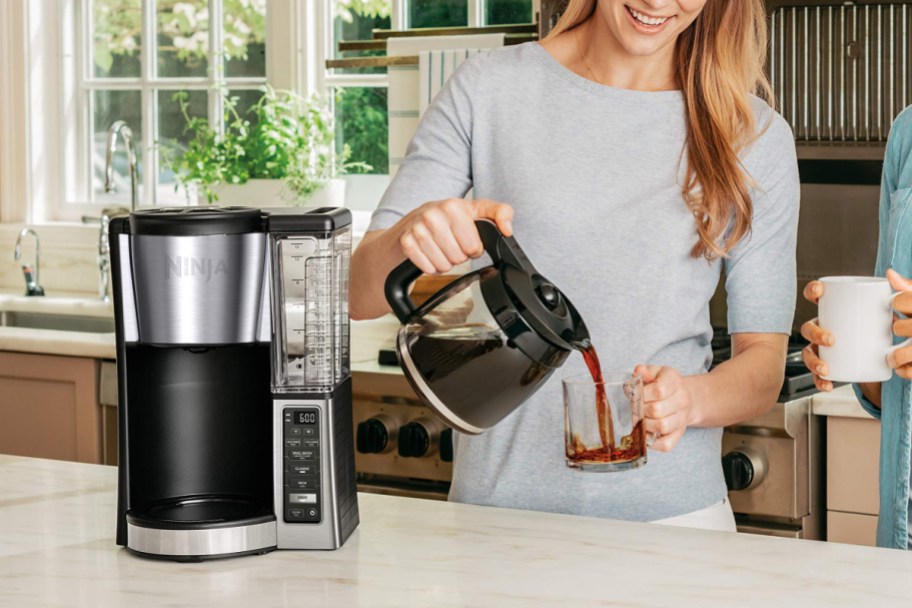 woman pouring coffee w/ ninja 12-cup coffee maker w: carafe